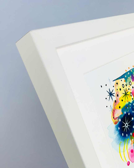 A close-up detail of the corner and edge of a small, chunky, white picture frame containing a colourful art print by Kate Elkington
