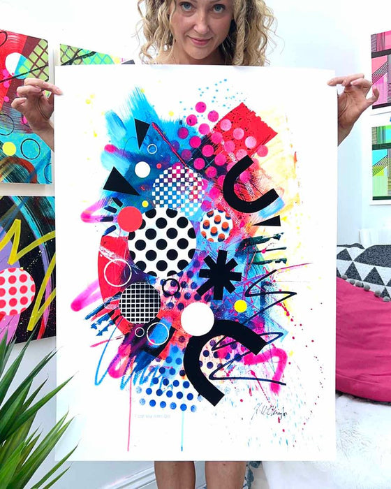 The artist Kate Elkington holding a large, A1 sized, vibrant, colourful abstract artwork featuring bold, graphic shapes, dynamic brushstrokes, and playful patterns. The composition includes splashes of neon pink, orange, and blue, layered with geometric elements such as dots, grids, and curved black lines, radiating energy and movement.