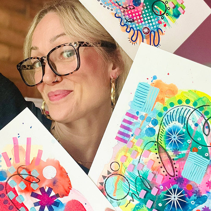 Artist Kate Elkington holding her colourful abstract 'Happy Doodle' art pieces with a blurred background