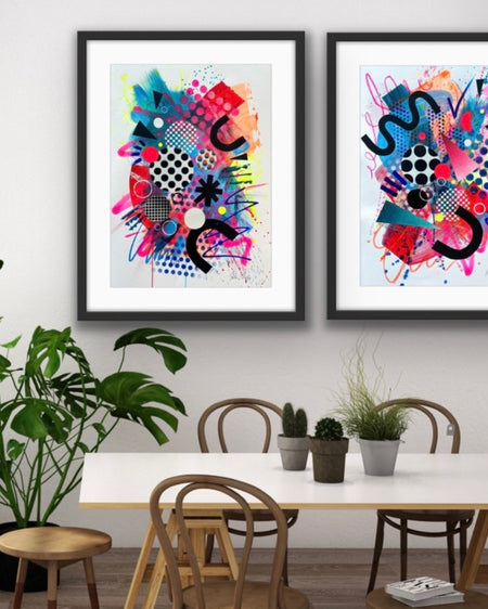 An interior with a long table and bentwood chairs and a set of two, black framed large, A1 sized, vibrant, colourful abstract artwork's by artist Kate Elkington on the wall, featuring bold, graphic shapes, dynamic brushstrokes, and playful patterns. The composition includes splashes of neon pink, bright red, orange, and blue, layered with geometric elements such as dots, grids, and curved black lines, radiating energy and movement.