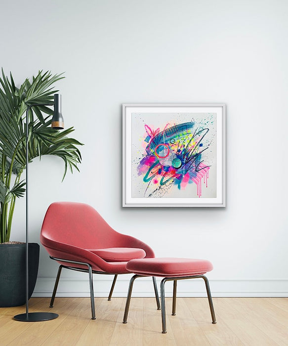 An interior with a plant and a pink chair with matching footstool. On the wall a white framed dynamic abstract artwork by Kate Elkington featuring bold splashes of neon pink, jade green, yellow, orange, and blue, combined with graphic circle shapes, stripes, black accents and white grid patterns. Expressive brush strokes, crayon scribbles and paint drips add movement and energy, creating a vibrant and playful composition that radiates joy and positivity.
