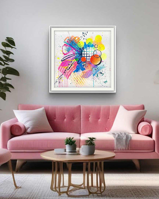 An interior with a pink sofa and a white, framed, dynamic abstract artwork by Kate Elkington featuring bold splashes of neon pink, yellow, orange, and blue, combined with graphic circle shapes, stripes, black accents and white grid patterns. Expressive brush strokes, crayon scribbles and paint drips add movement and energy, creating a vibrant and playful composition that radiates joy and positivity.