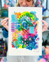The artist Kate Elkington holding an A3 sized vibrant abstract giclée art print, featuring a playful mix of shapes and colours. Greens, yellows, blues, indigo and pinks are blended with soft washes of watercolour, overlaid with whimsical patterns like dots, stars, and swirls. Free-flowing lines and dynamic brushstrokes create a sense of movement, while geometric elements such as squares and circles add structure.