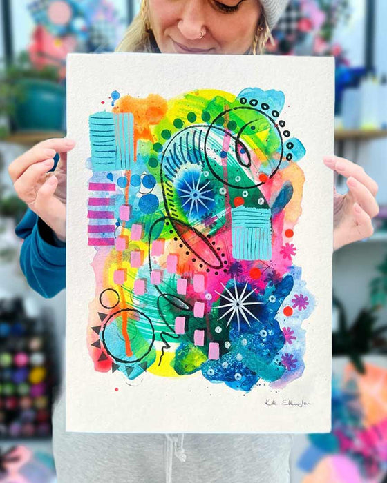 The artist Kate Elkington holding an A3 sized vibrant abstract giclée art print, featuring a playful mix of shapes and colours. Greens, yellows, blues, indigo and pinks are blended with soft washes of watercolour, overlaid with whimsical patterns like dots, stars, and swirls. Free-flowing lines and dynamic brushstrokes create a sense of movement, while geometric elements such as squares and circles add structure.