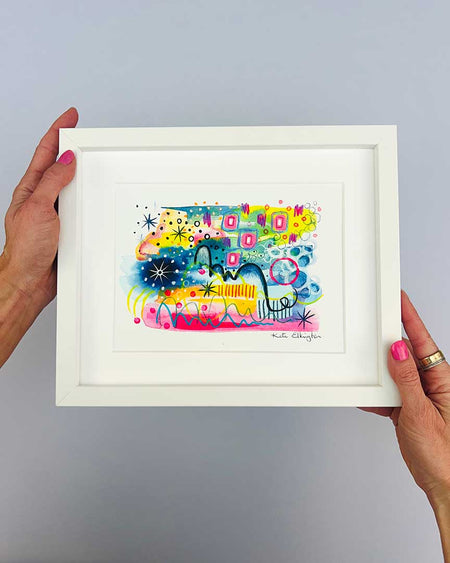 The artist Kate Elkington's hands holding a small, white, framed vibrant abstract giclée art print, featuring a playful mix of shapes and colours. Golden yellows, blues, indigo and pinks are blended with soft washes of watercolour, overlaid with whimsical patterns like dots, stars, and swirls. Free-flowing lines and dynamic brushstrokes create a sense of movement, while geometric elements such as squares and circles add structure. The overall composition uplifting and joyful