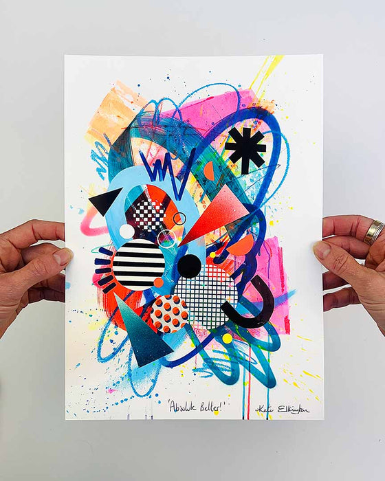The artist Kate Elkington's hands holding a vibrant abstract artwork featuring a dynamic mix of bold shapes, patterns, and colours. The composition includes overlapping circles, triangles, and lines in neon pinks, blues, oranges, and yellows, accented with stripes, polka dots, and grid designs. The piece radiates energy and playful creativity.
