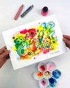 The hands of the artist Kate Elkington holding an A4 sized vibrant abstract giclée art print in landscape orientation, featuring a playful mix of shapes and colours. Bright yellows, oranges, blues, greens, and pinks are blended with soft washes of watercolour, overlaid with whimsical patterns like dots, stars, and swirls. Free-flowing lines and dynamic brushstrokes create a sense of movement, while geometric elements such as squares and circles add structure. The overall composition is uplifting and joyful.
