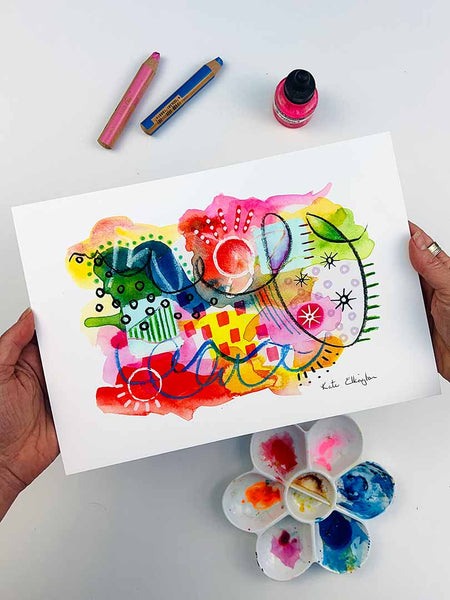 The hands of the artist Kate Elkington holding an A4 sized vibrant abstract giclée art print in landscape orientation, featuring a playful mix of shapes and colours. Bright yellows, reds, blues, greens, and pinks are blended with soft washes of watercolour, overlaid with whimsical patterns like dots, stars, and swirls. Free-flowing lines and dynamic brushstrokes create a sense of movement, while geometric elements such as squares and circles add structure. The overall composition is uplifting and joyful.