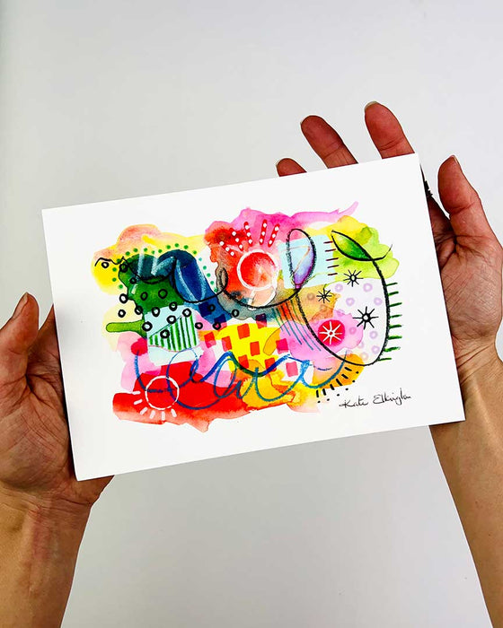 The hands of artist Kate Elkington holding an A5 sized vibrant abstract giclée art print in landscape orientation, featuring a playful mix of shapes and colours. Bright yellows, reds, blues, greens, and pinks blended with soft washes of watercolour, overlaid with whimsical patterns like dots, stars, and swirls. Free-flowing lines and dynamic brushstrokes create a sense of movement, while geometric elements such as squares and circles add structure. The overall composition is uplifting and joyful.