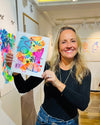 Woman holding a colorful abstract painting in an art gallery.