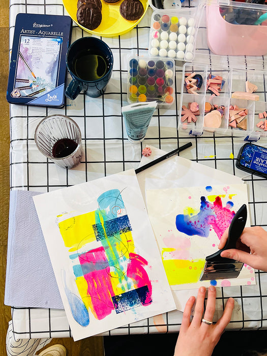 Artistic setup with watercolor paintings, supplies, and a person painting on paper.
